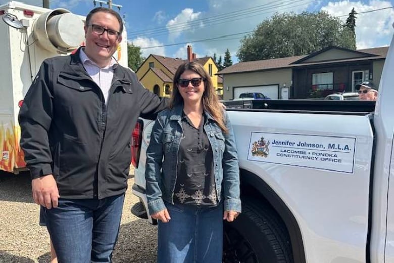 a tall man and a short woman stand by a pickup truck.