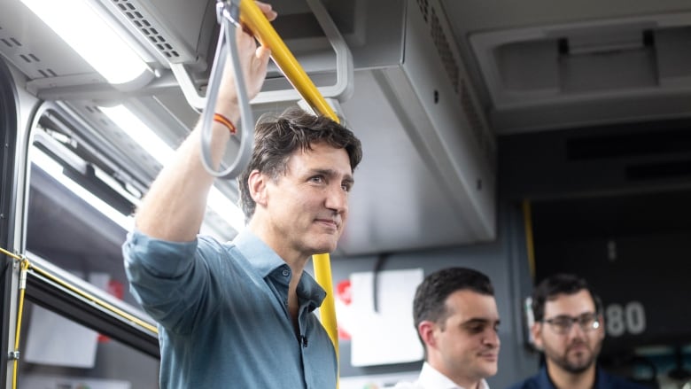 A man in a pale blue shirt hangs on to a strap while standing in a bus.