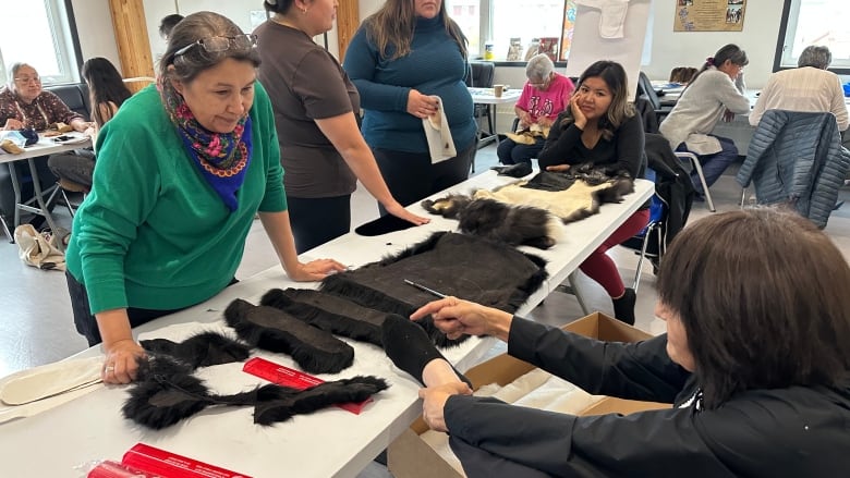 Women gather around a table where a pelt is being cut up.