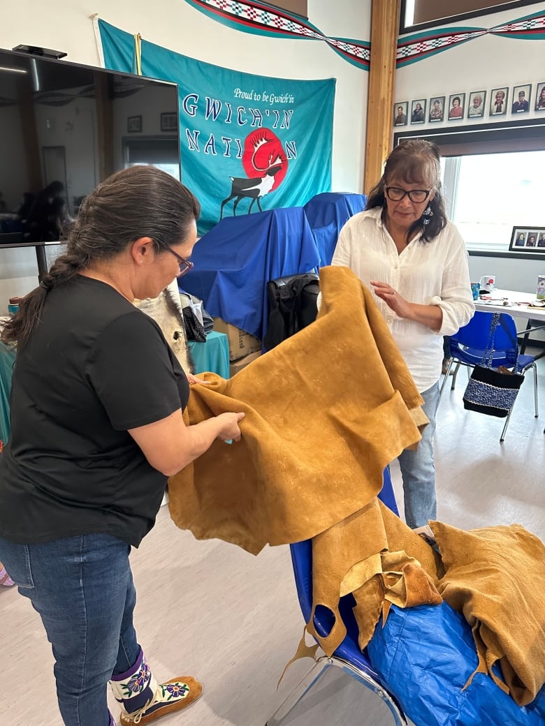 Two women hold up a large piece of leather.