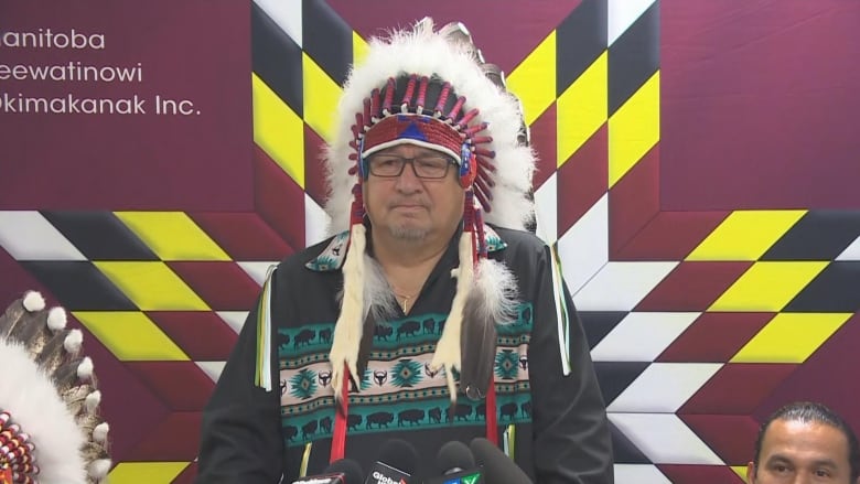 A man in a headdress speaks at a podium.