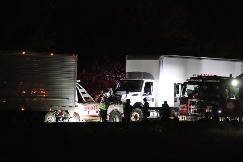 A crashed tow truck and container truck are seen at night.