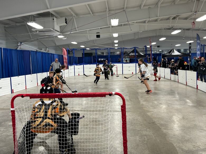 A group of young people play hockey indoors at a sports complex.