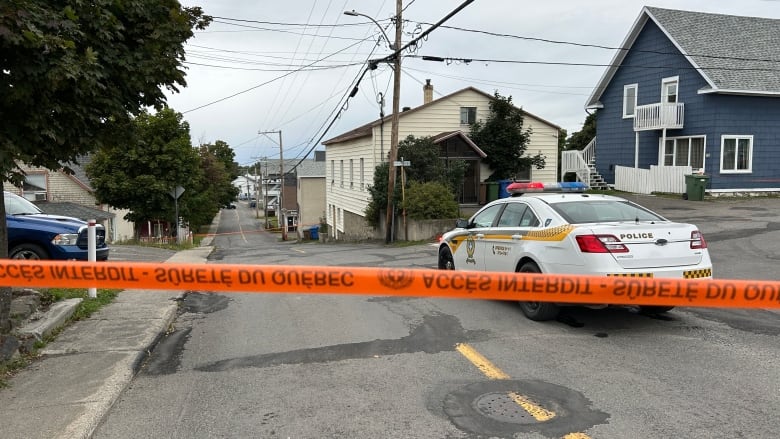 Police tape and a police car blocking off a residential street. 