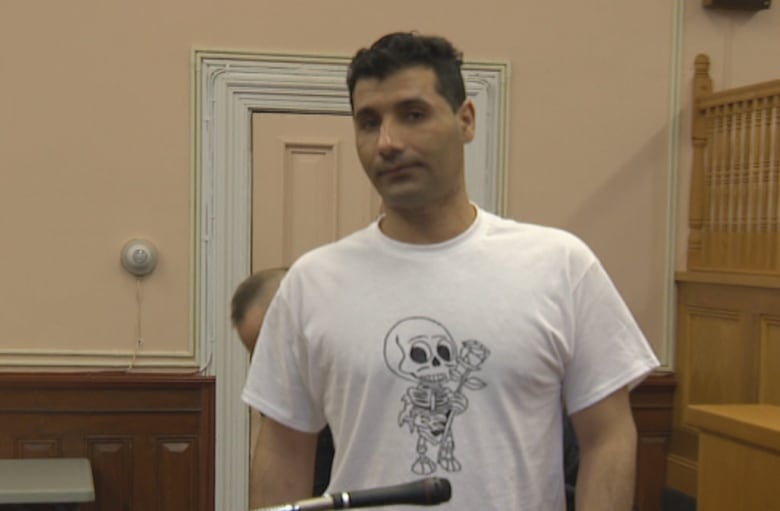 a man standing in a courtroom, wearing a white t-shirt.