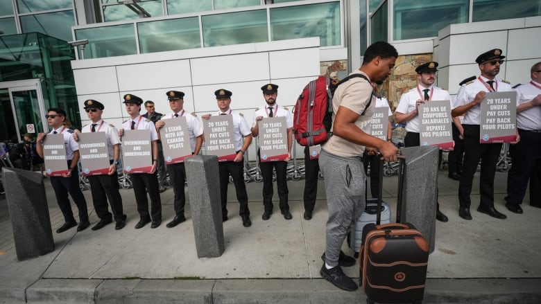 A traveller passes a line of pilots holding signs.