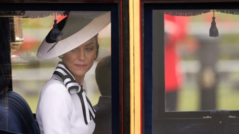 A woman in a white dress and white hat sits in the back of a horse-drawn carriage.