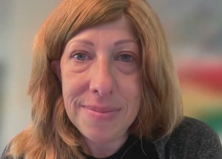 A woman with long, red hair looks into the camera.