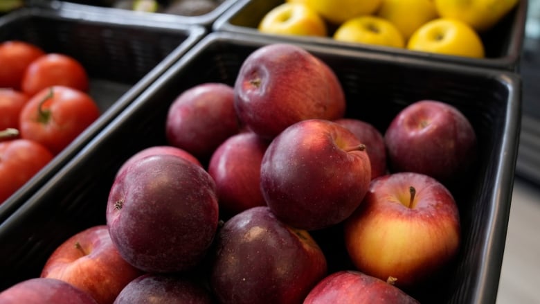 Red apples lie in a black container at a market. 