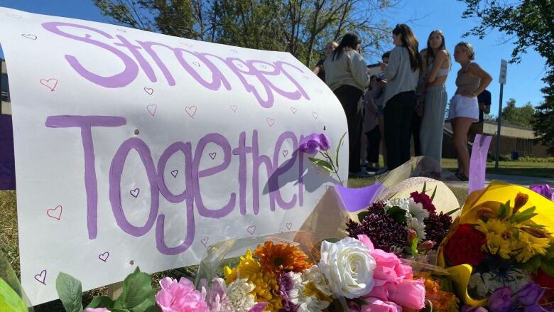 Flowers and posters sit on the grass while a group of students stand nearby.