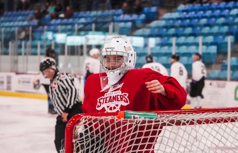 A female hockey player wearing a steamers shirt stands in front of the goal net