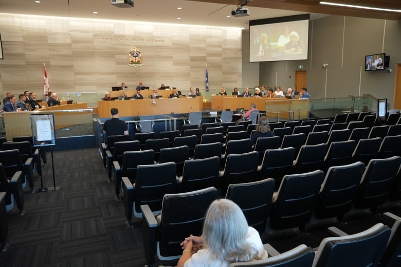 A person sits inside of an empty gallery while city councilors and administration discuss a budget. 