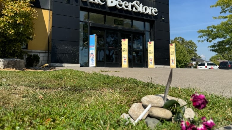 Rocks, flowers and a feather make up a small memorial on the grass in front of The Beer Store.