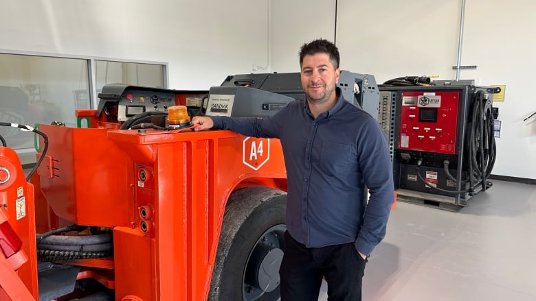 A man standing next to an orange piece of heavy machinery.