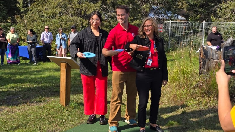 Three people with frisbees at a disc golf course.