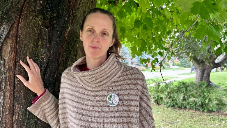 A woman stands by a tree. 