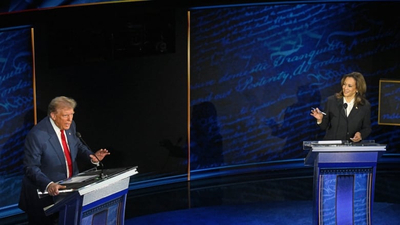 Donald Trump speaks into a microphone on the left side of a stage opposite Kamala Harris gesturing toward him from behind a podium.