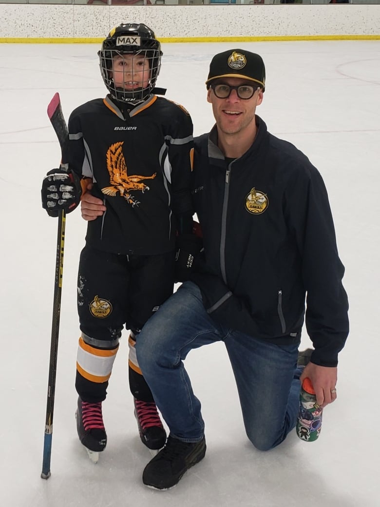 Man kneeling with arm around boy in hockey gear