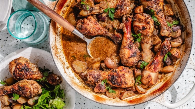 Overhead shot of a white pot with cooked chicken drumsticks and potatoes. A drinking glass and a bowl with the chicken sit next to the pot. 