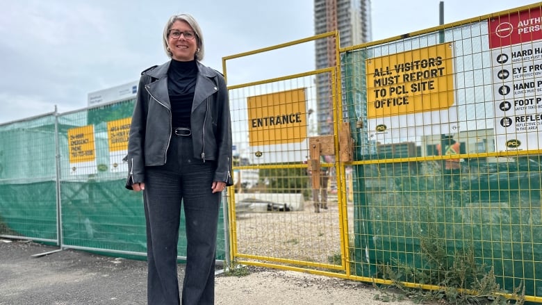 A woman stands in front of a construction site with a tower in the background.