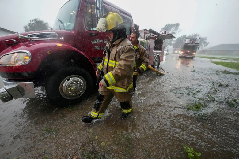 Firefighters walk through a flooded street.