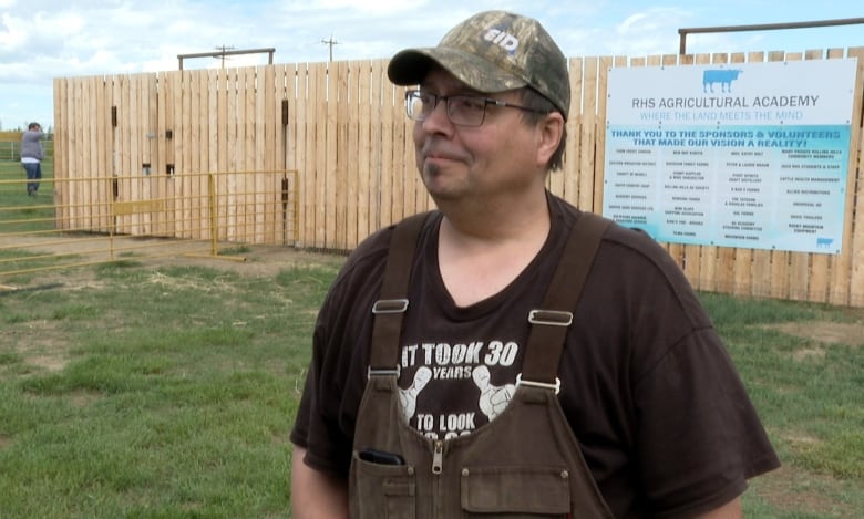 A man in overalls and a baseball cap stands in a field. 