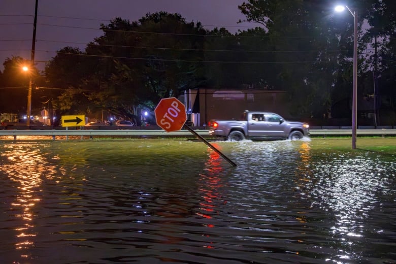 A pickup truck drives along a flooded street at night. A stop sign is bent at an angle.