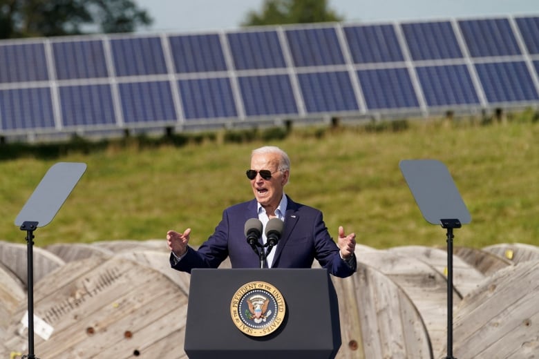 A person speaks at a podium with solar panels in the background.