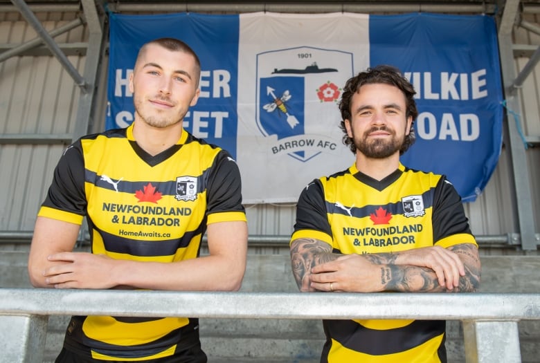 Two men wear yellow and black striped soccer jerseys with short sleeves. 