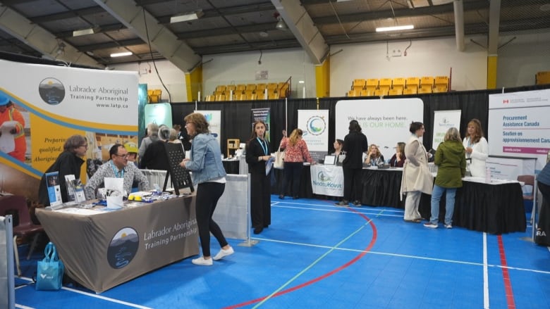 A series of booths and tables are set up inside a gymnasium. People are walking through and perusing the tables.