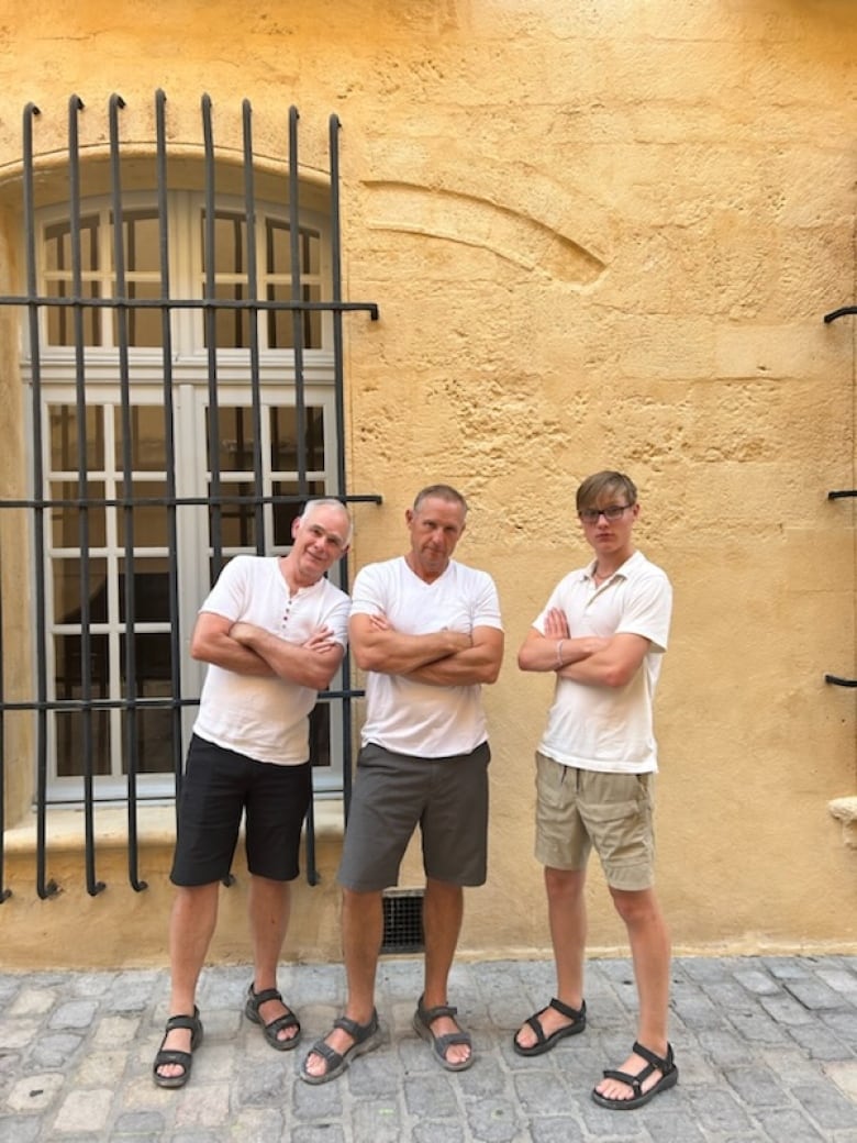 Three men wearing white T-shirts fold their arms.