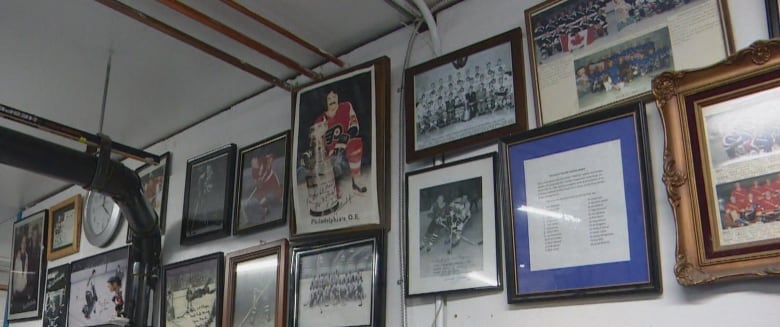 A white wall with old photos of hockey players and teams. Some pipes line part of the ceiling.