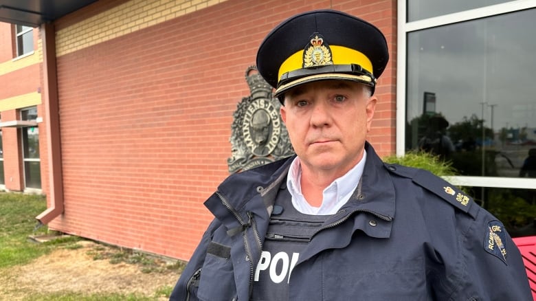 A uniformed police officer is standing in front of brick building.