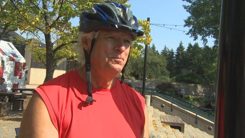 A man wearing a red tank is standing while still wearing a blue and white helmet.