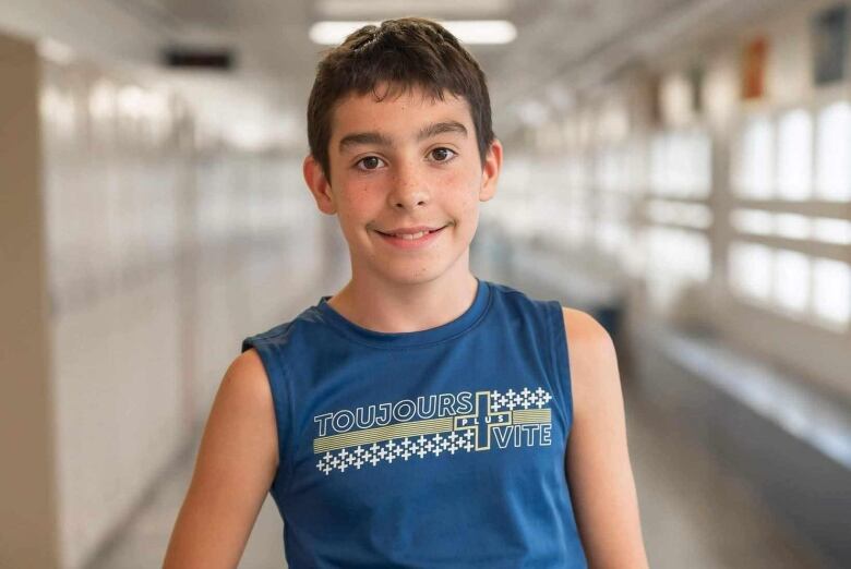 A picture of a boy smiling at the camera. Behind him is a school hallway.