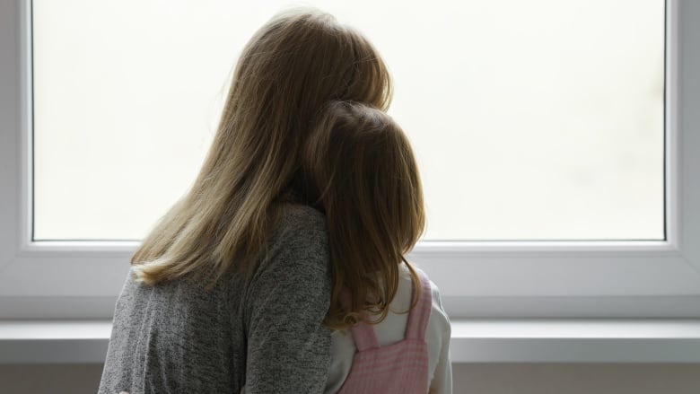 Young adult mother and daughter together looking out from window at hom