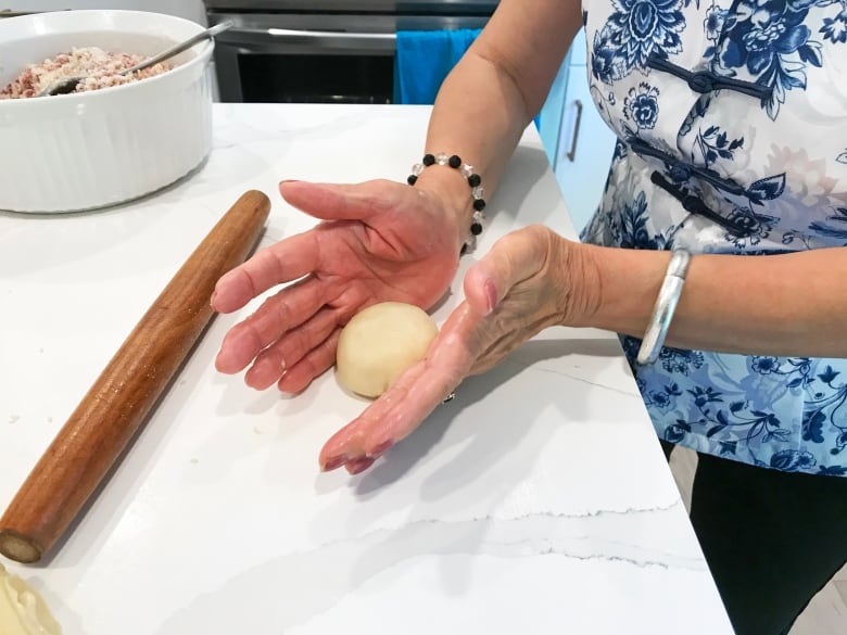 A woman rolls dough with her hands to make mooncakes.