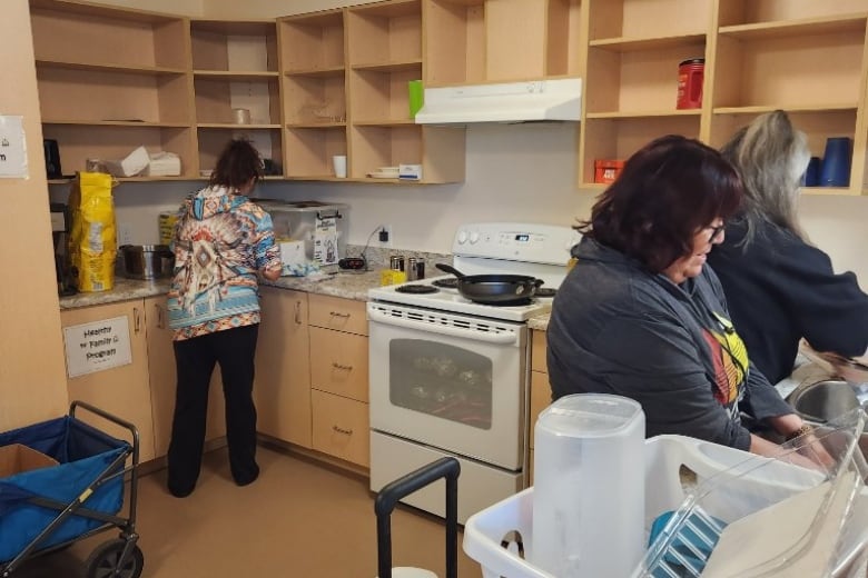 Three women cooking and cleaning in community kitchen.