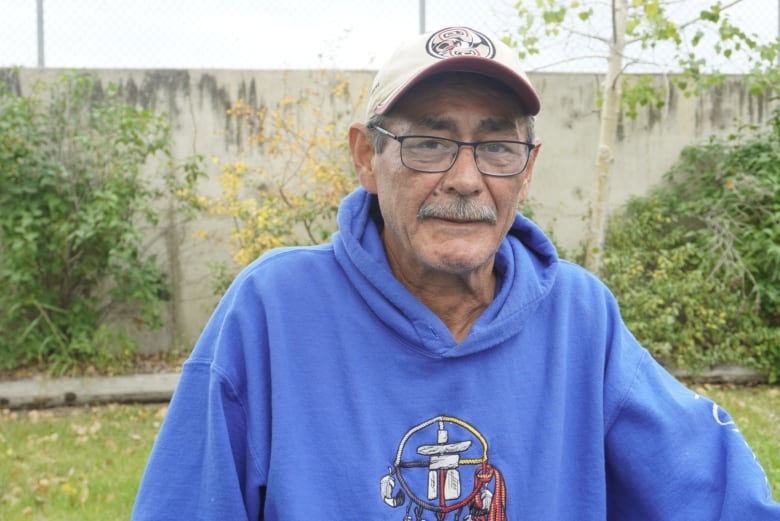 Man in blue hoodie and baseball cap sits outside