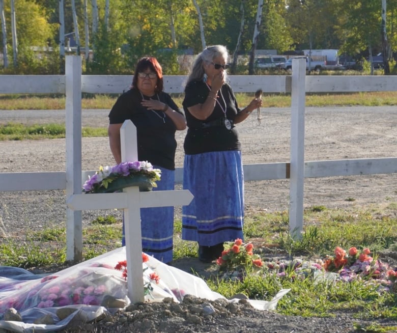 Women in matching skirts stand in cemetery. 