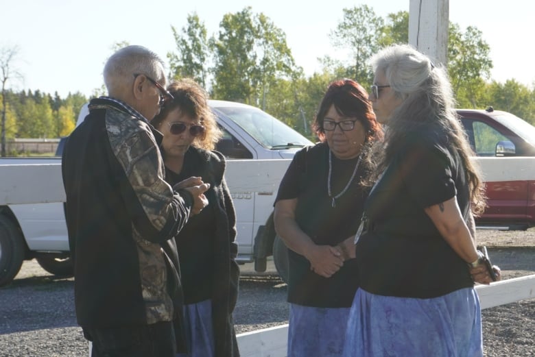 Man and three women stand solemnly in a circle with their heads down.