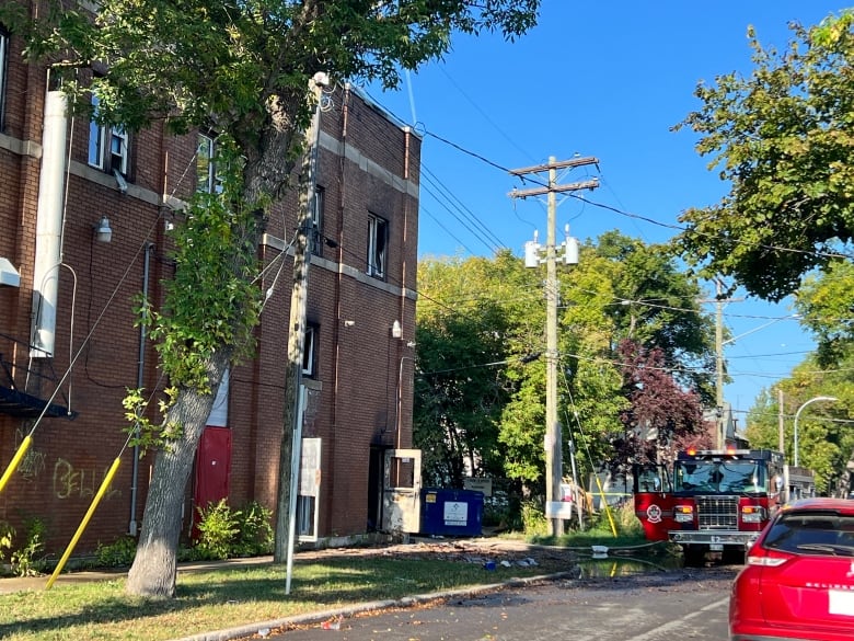 A fire truck is parked outside a building that was on fire. Some of the windows in the building are smashed and the back door is open. 