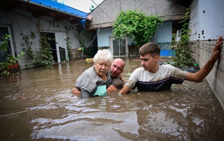 Three people stand in floodwaters. 