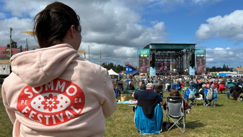 Woman with pink hoodie looking toward an outdoor music stage.