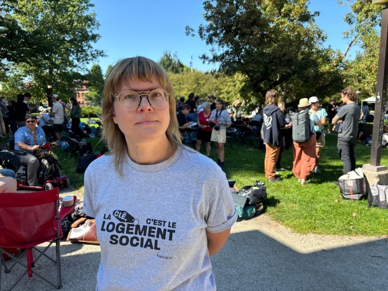 A woman looks into the camera wearing a shirt that reads, 