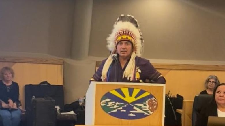 An Indigenous man standing a podium wearing a headdress.