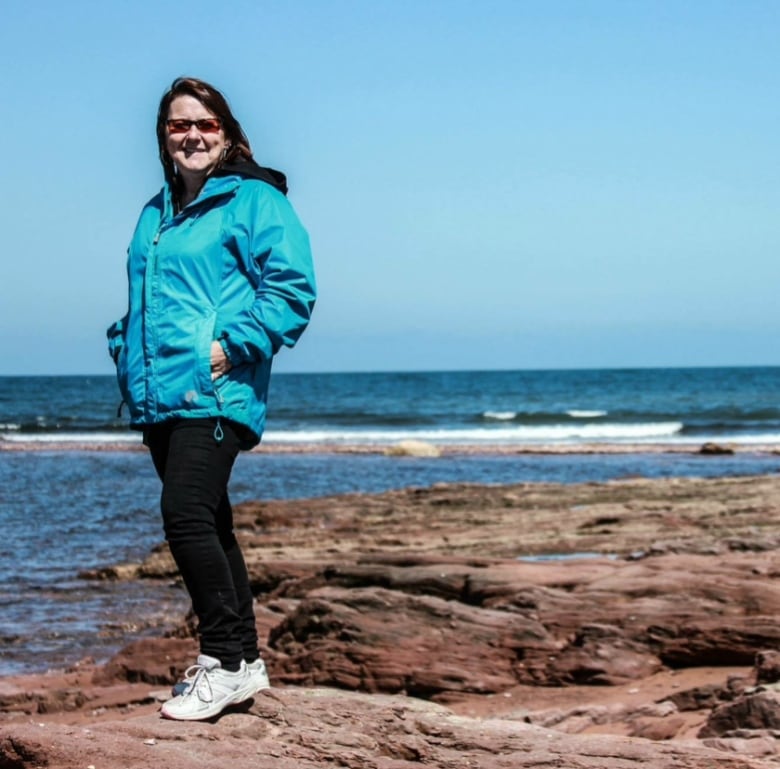 Woman in blue jacket standing on rocks by the sea.