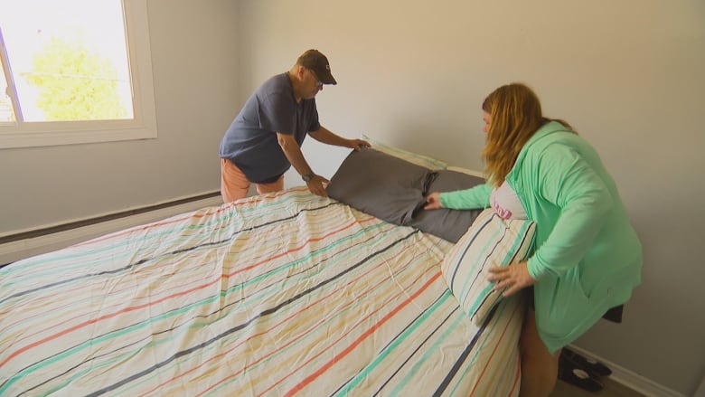 Two people stand on oppposite sides of a bed and adjust pillows