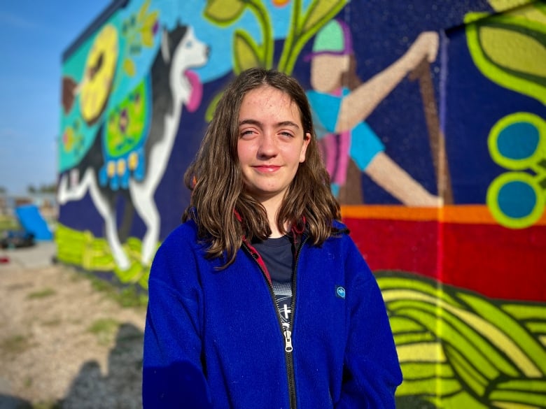 A young poses for a photo in front of a mural outside. 