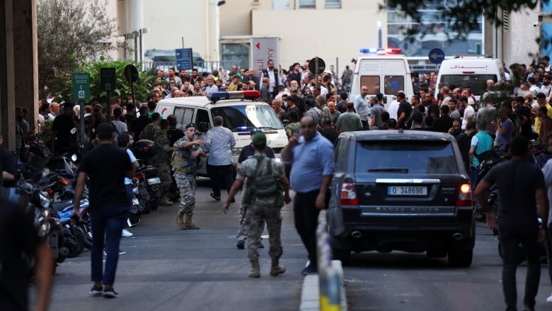 An ambulance drives around hundreds of people gathered outside a hospital.